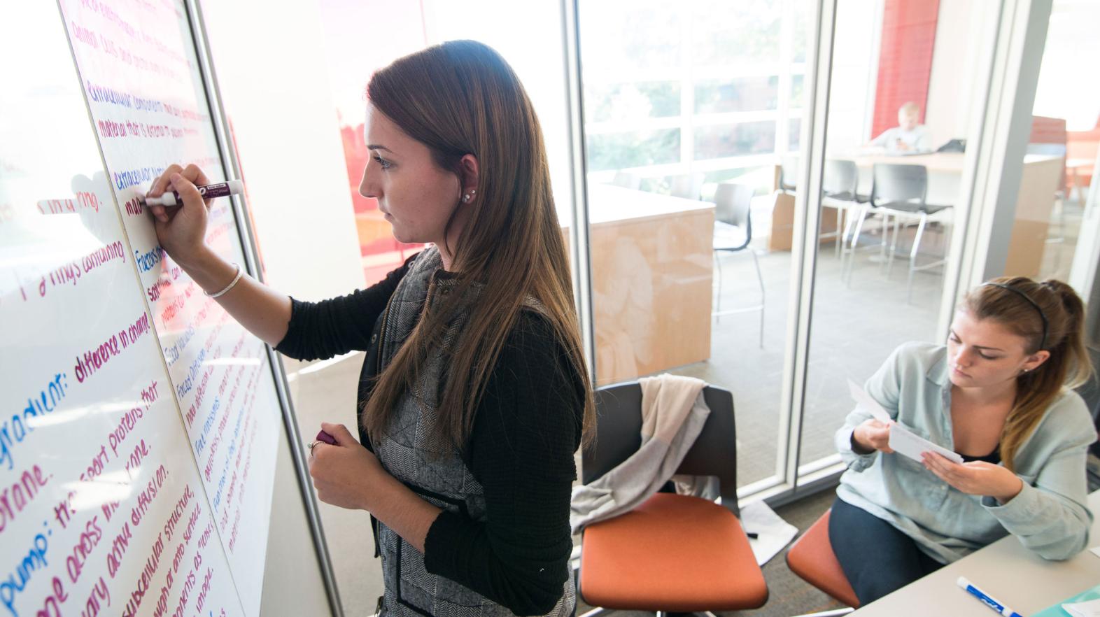 A female student takes notes on the white boards in the learning commons